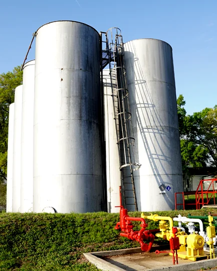 Large vertical bulk fuel storage tanks with piping and pump system at an industrial facility.